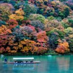 kyoto_japan_-_nov_23_2012_traditional_tourist_boat_pass_on_the_emerald_color_katsura_river_along_the_beautiful_autumn_leaves_in_the_cold_tone_arashiyama_kyoto_japan
