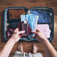 Preparing for travel in new normal. Man packing passport, face masks and hand sanitizer. Themes personal protection and flight rules during coronavirus pandemic.